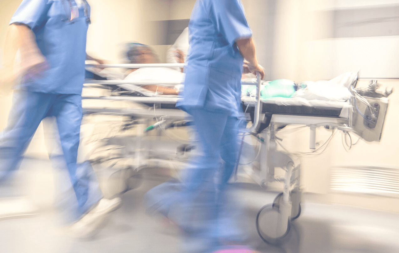 Nurses and hospital professionals in blue scrubs rolling a patient in a hospital bed down a hallway